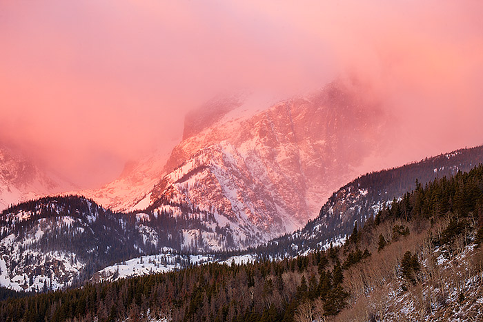 Hallet Peak basks in the warm light of sunrise as snow and wind blow over the peak. Hallet Peak is one of the most recognizable features in Rocky Mountain National Park. Hallet make for a great subject for photography in the park. Technical Details: Canon EOS 1Ds III, 70-300mm F4-5.6 L