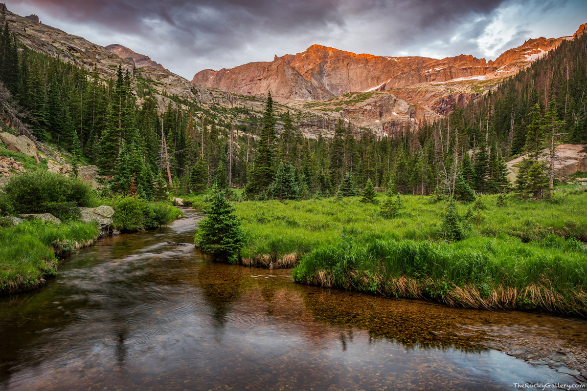 Storm clouds roil over the top of Chiefs Head Peak along a placid Glacier Creek on a July morning in Rocky Mountain National...