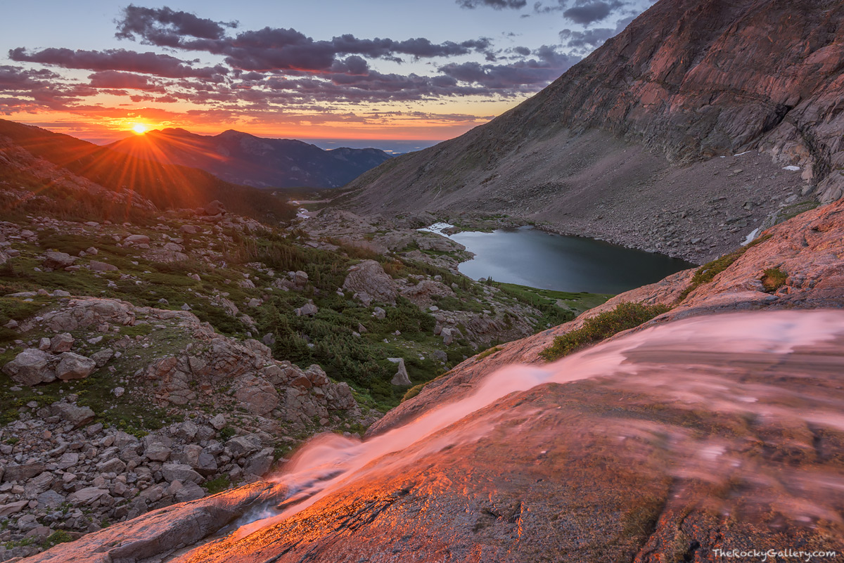 The sun breaks the horizon of Colorado's high plains and crests the Twin Sisters off in the distance. Columbine Falls just below...