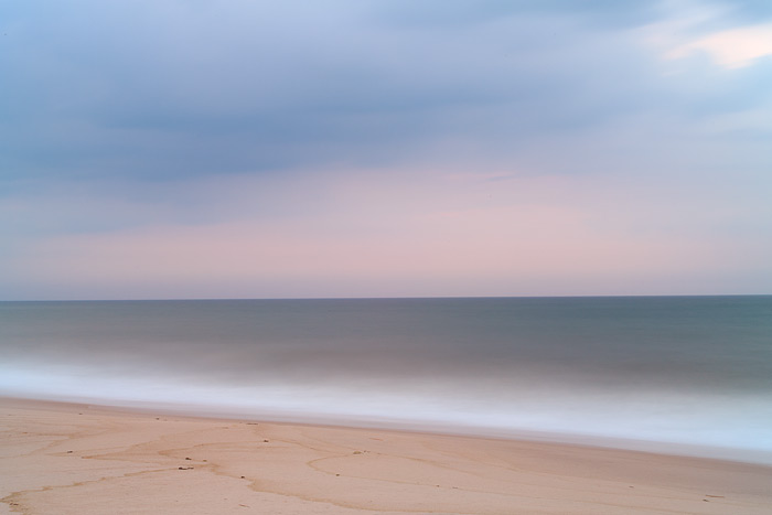 Pastel colors form in the sky and ocean above Dune Beach in Southampton, New York. Waves crash along the shoreline on a peaceful...