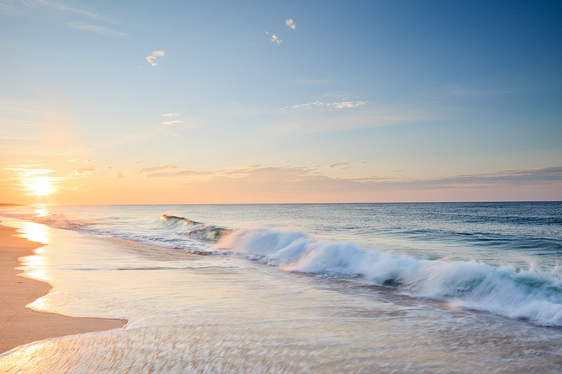 The sun rises over Dune Beach in Southampton, New York. Waves crash along the shore's of the Beach and the few passing clouds...