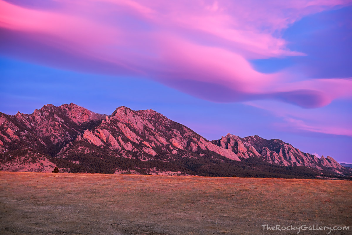 A beautiful pastel sunrise unfolds over the Flatirons of Boulder, Colorado on a mild February morning. Winds aloft create a lenticular...