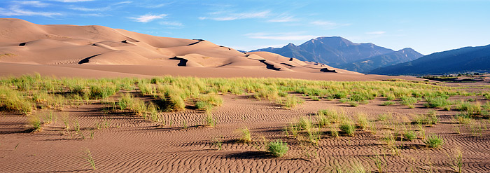 Wispy clouds float over Colorado's highest dunes in the San Luis Valley. The Grass along Medano creek are green and the redish...