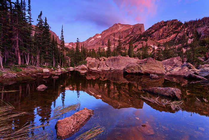 Soft diffused sunrise alpenglow light filters over Hallet Peak and the rocky shore line of Lake Haiyaha in Rocky Mountain National...