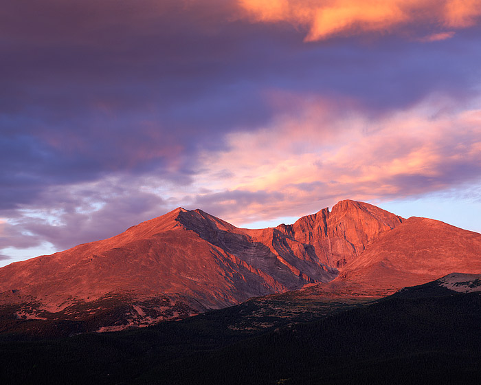 A brilliant magenta and red sunrise illuminates Longs Peak and Mount Meeker from the Twin Sisters. It's a serene and windless...