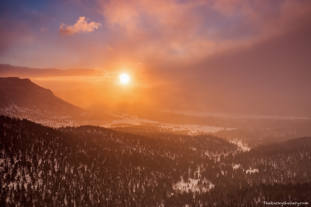 The morning sun crests the horizon over Rocky Mountain National Park and illuminates the sky and snow in vibrant reds and oranges...