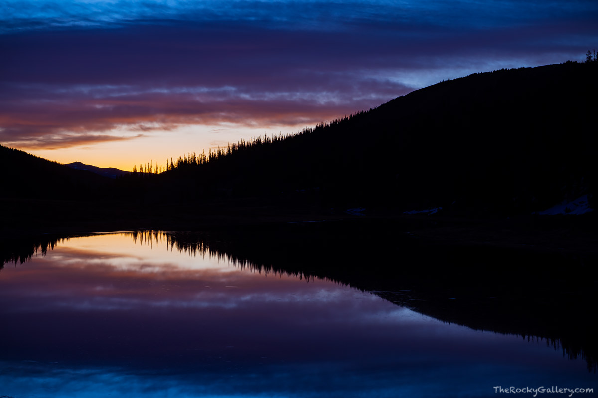 Predawn light illumintaes the skies over a placid Milner Lake stradling the Continental Divide seperating the east and west side...