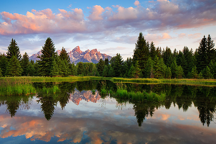 Clouds drift over the Grand Tetons at sunrise from Schwabacher Landing. Sunrise illuminates the bottom of the clouds in a subtle...